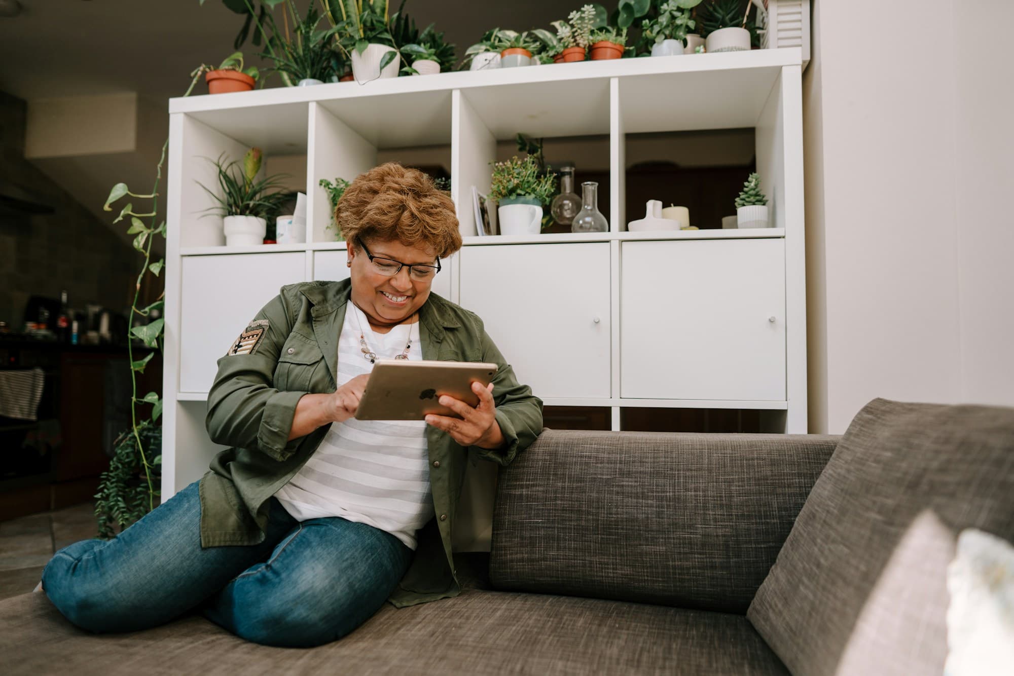 A member reading on a tablet at home, surrounded by plants